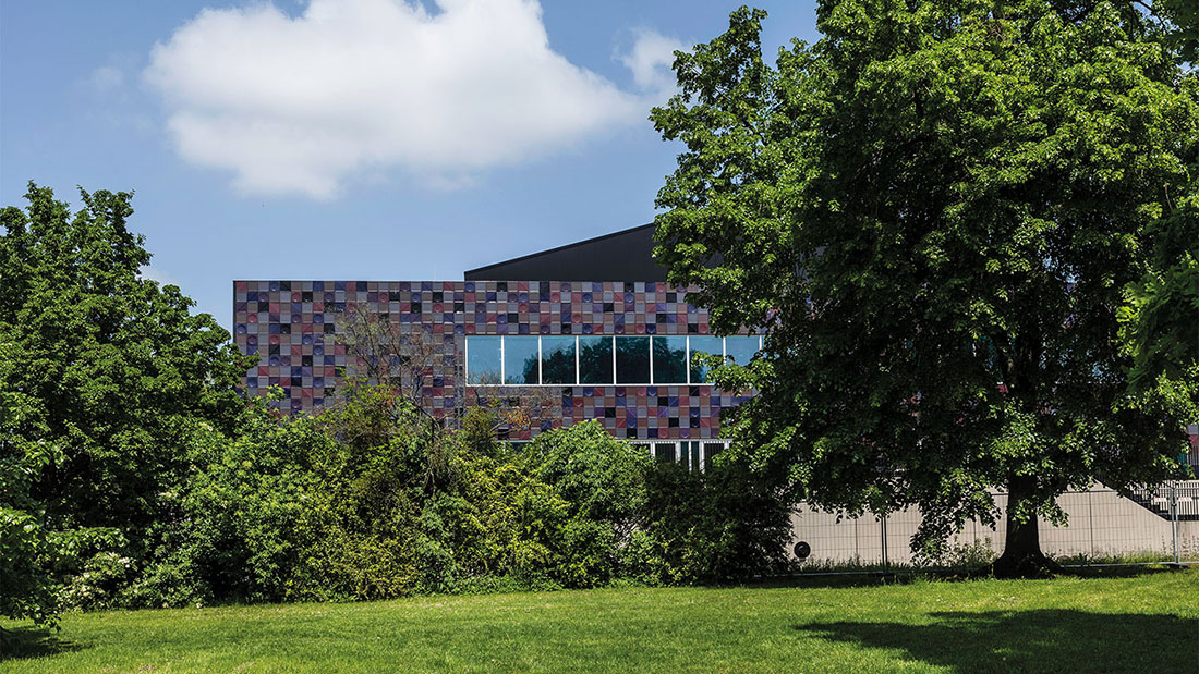 Moderne Stadthalle Göttingen mit bunter Fassadenverkleidung, umgeben von Bäumen und Rasen