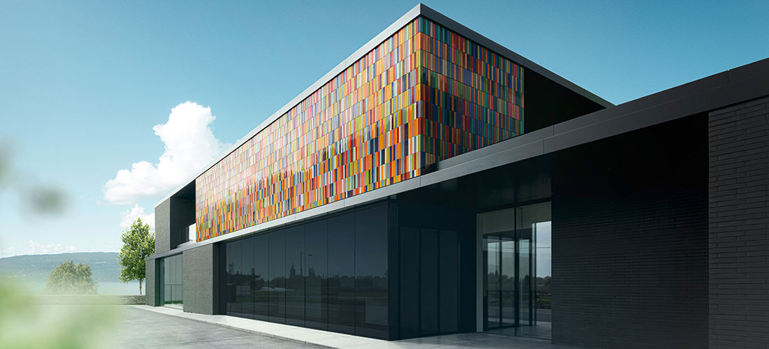 Modernes Gebäude mit einer Fassade aus bunten rechteckigen Paneelen und großen Glasflächen unter blauem Himmel