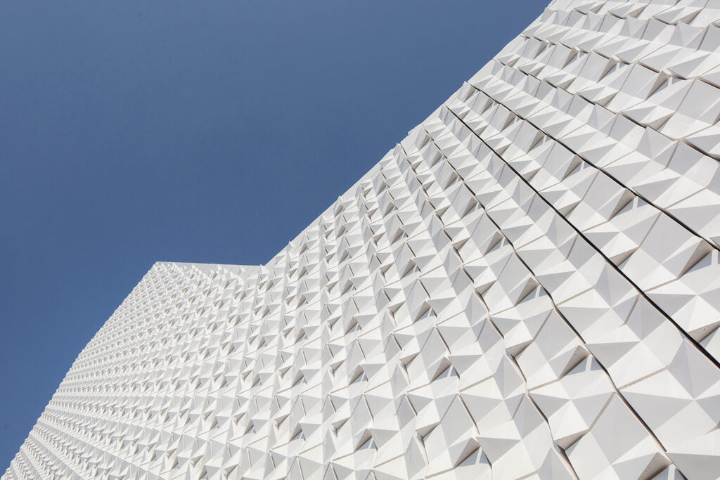 Fassadendetail der Kirche St. Michael in Poing mit weißer, geometrisch strukturierter Oberfläche aus dreidimensionalen, pyramidenartigen Fassadenkacheln vor klarem, blauem Himmel