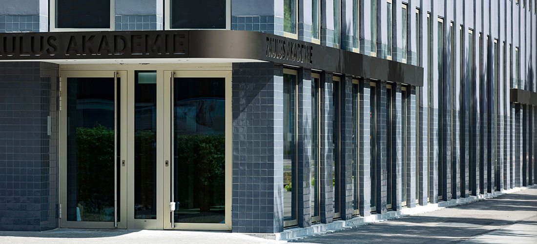 Eingang der Paulus Akademie mit großen Fenstern und Schriftzug über dem Vordach