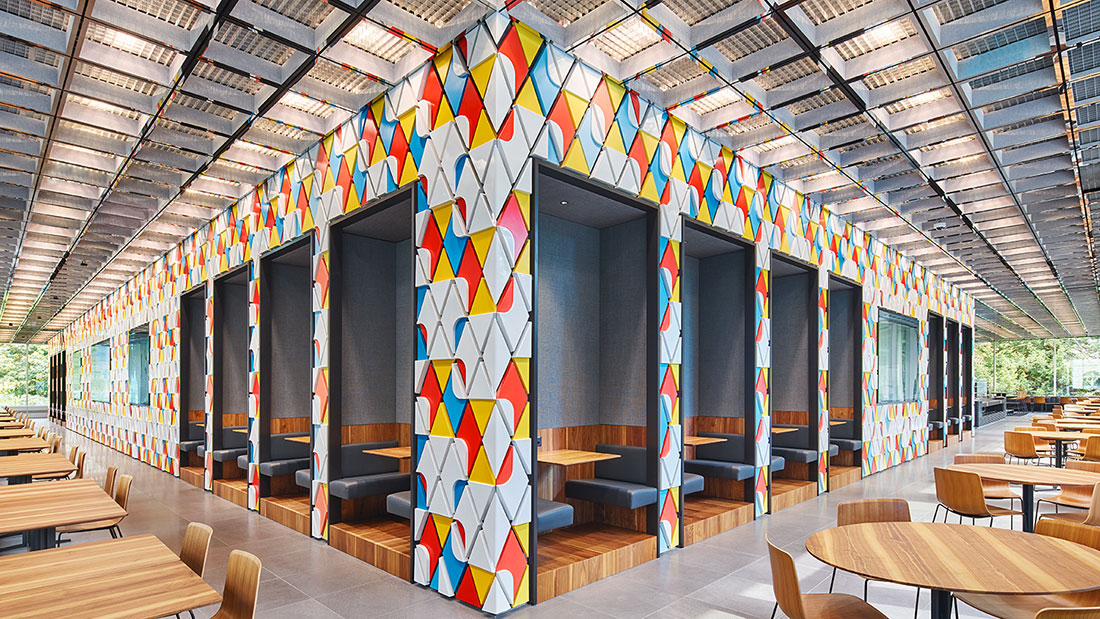 Mehrere Sitznischen mit blauen Polstern und Holztischen, umgeben von einer Wand mit buntem, geometrischem Muster